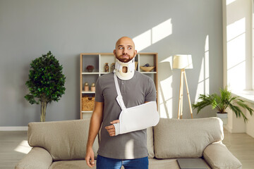 Unhealthy young man in gypsum on broken hand and bandage on neck having rehabilitation period at home. Unwell guy in plaster on arm and protective collar for back fracture. Rehab, healthcare.