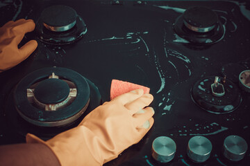 A woman in yellow gloves is cleaning the surface of a gas stove. Daily kitchen cleaning duties....