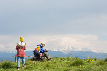 Fototapeta na wymiar family father and children sit and eat on background of nature - mountain landscape. travel with kids.