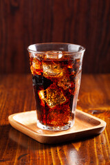 glass of cold cola soft drink with ice on wooden background