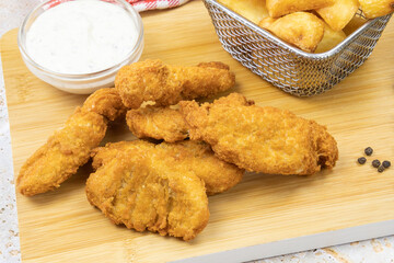 potato with cooked chicken nuggets on a wooden board with a pot of sauce