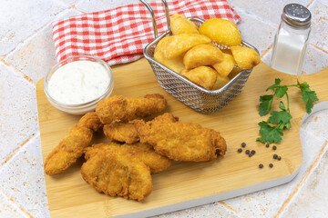 potato with cooked chicken nuggets on a wooden board with a pot of sauce