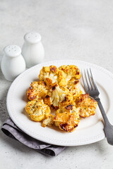 Baked crispy spicy cauliflower on white plate. Cooking healthy food concept.