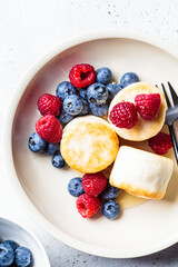 Tofu pancakes with raspberries, blueberries and syrup in white bowl, gray background. Vegan food concept.