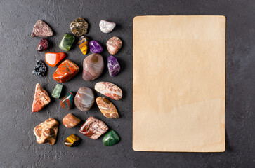 Mineral stones and an old piece of paper. Black concrete background. The concept of using minerals in astrology and alternative medicine. Copy space.
