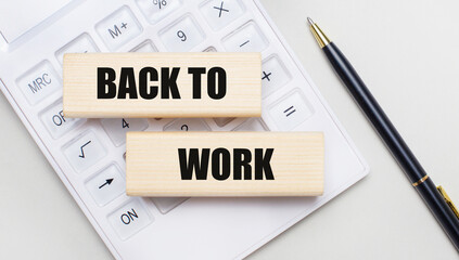 Wooden blocks with the BACK TO WORK Iie on a light background on a white calculator. Nearby is a black handle. Business concept