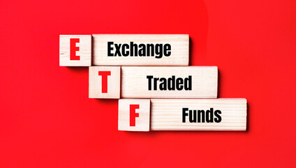 On a bright red background, wooden cubes and blocks with the text ETF Exchange Traded Funds. Manufacturing of wooden toys.