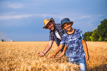 Happy father and son are standing in their grown wheat field before harvest.