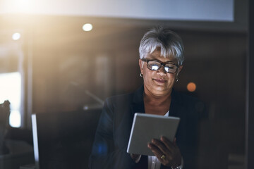 Digital business dealings after dark. Shot of a mature businesswoman using a digital tablet late at night in a modern office.