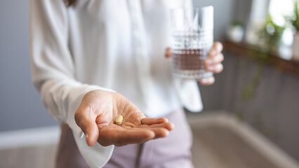 Close up sick woman holding glass with water and pill in hands, suffering from headache, flu or depression, taking antibiotic, antidepressant or painkiller medication, emergency treatment concept