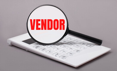 On a gray background, a white calculator and a magnifying glass with the text VENDOR. Business...