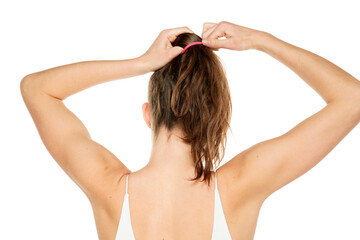 Rear view of a young woman tying her long wavy hair on a white background