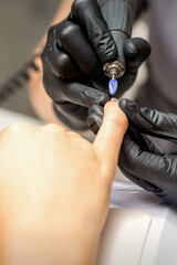 Manicure master uses electric nail file machine in a nail salon, close up