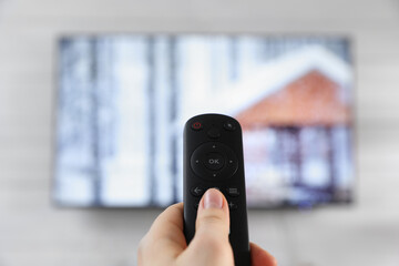 Woman with remote control watching TV at home, closeup