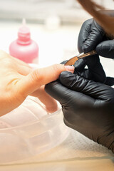Close up professional manicurist master holding customer hand while using a cuticle pusher in a...