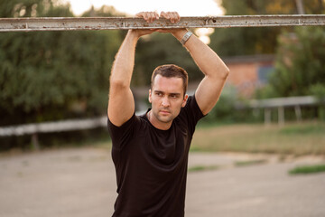 Portrait of a smiling young male athlete leaning on horizontal bars, resting after running