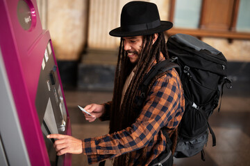 Handsome hipster guy is buying bus ticket at self service vending machine on the station.