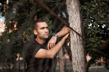 Portrait of a young handsome man with unshaven bristles in a black T-shirt leaning on a mesh fence