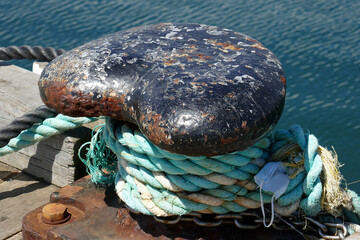 Fototapeta na wymiar mooring ropes around an old mooring bollard-trapped in the coils is a face mask re covid.