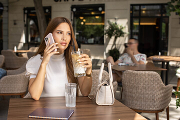 Young woman drinking coffee alone talking on her smartphone