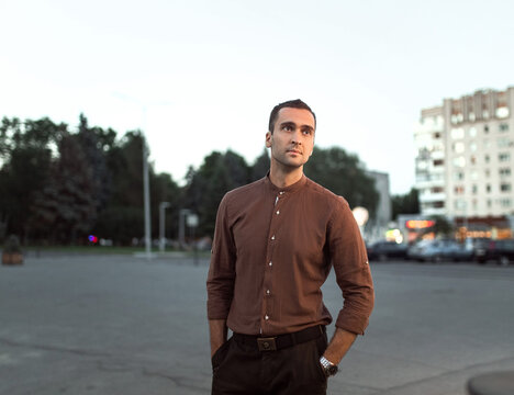 portrait of a young handsome man with unshaven bristles in a brown shirt on the background of the evening city