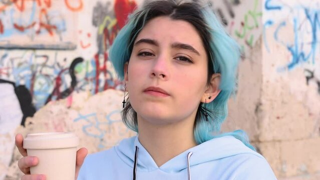 Teenage girl in blue oversize hoodie drinking coffee to go. Blue haired teen girl staying outdoors near graffiti wall. Mockup, head shot. Hipster and adolescence concept