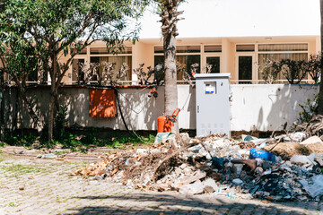 Garbage rubble pile in front of the residential building. Fuse box surrounded with litter. Household rubbish debris scattered outside the residential district.