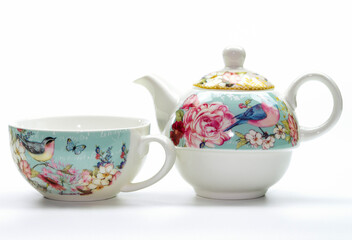 Porcelain teapot and cup with flower and bird pattern on a white background