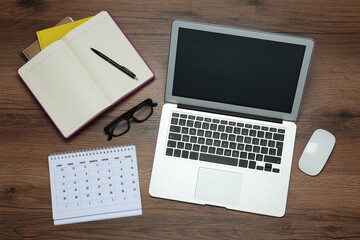 Modern laptop, glasses and office stationery on wooden table, flat lay. Distance learning