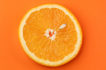 Round slice of orange with pit on orange background