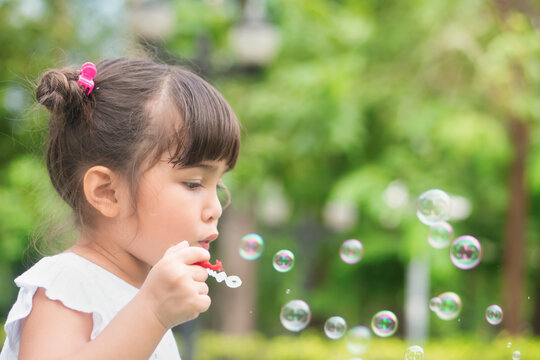 Cute little girl playing, blowing bubble in outdoor summer city park