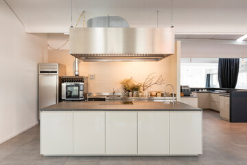 Front view of professional kitchen with island and large hood. Behind there is an oven, with a...