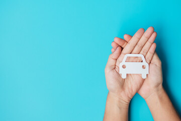 Hand holding paper Car cutout on blue background. Vehicle insurance, warranty, Automobile rental, Transportation, Maintenance and repair concept