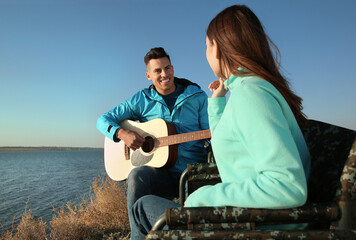 Couple with guitar resting in camping chairs near river on sunny day