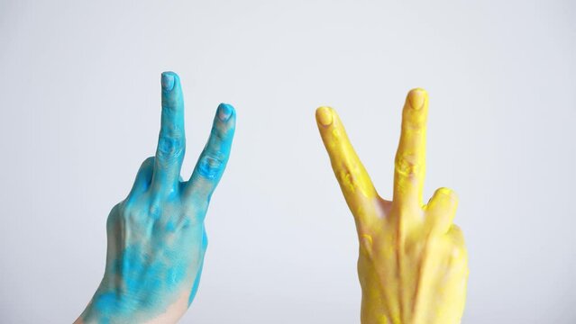 Closeup view 4k stock video footage of two female hands painted in blue and yellow colors of ukrainian national flag. Happy adult woman showing V letter or victory sign or symbol gesture both hands