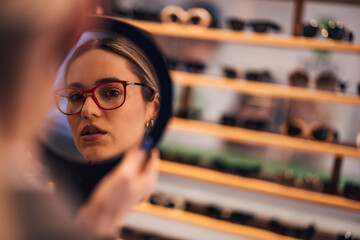 Girl looking at herself, holding a mirror, trying glasses.