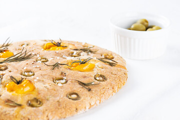 Homemade focaccia with tomatoes, olives, rosemary and spices on a light table. Gluten free, healthy food, vegan.