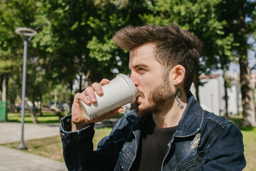 Young man wearing casual clothes drinking coffee. He is looking away while drinking coffee.