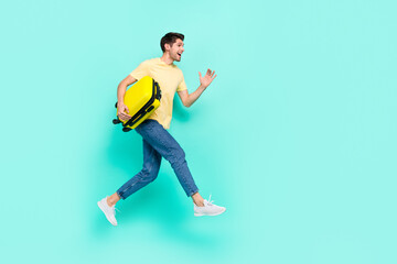 Fototapeta na wymiar Full size photo of cool brunet guy run with bag wear t-shirt jeans shoes isolated on teal background