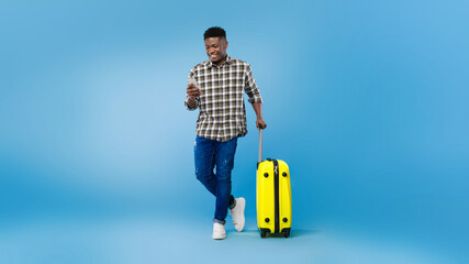 Handsome young black man with suitcase using mobile phone, booking summer vacation tourist trip...