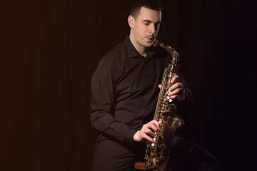 Young man playing saxophone on dark background. Space for text