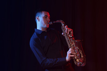 Obraz na płótnie Canvas Young man playing saxophone on dark background