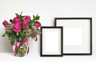 Bouquet of pink rose flowers in a glass vase and brown empty frames on white background