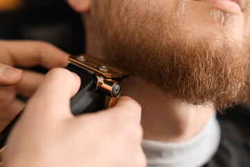 Professional hairdresser working with bearded client in barbershop, closeup