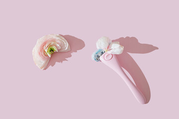 A pink women's razor shaving with white petals and a half ranunculus flower creative flat lay. Beauty hygiene routine. Body positivity movement and gender inclusiveness idea. Pink background.