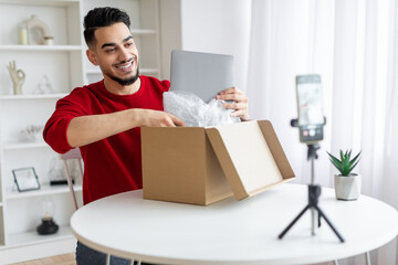 Handsome Arab Male Blogger Unboxing Parcel With Laptop On Camera