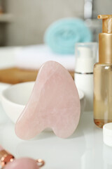 Rose quartz gua sha tool and cosmetic products on white table indoors