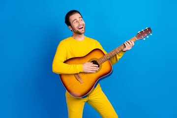 Portrait of attractive cheerful guy playing guitar singing pop single isolated over bright blue...