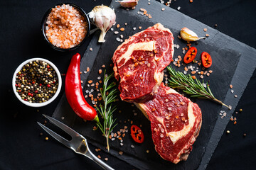 raw meat on a black board with chili, papper, garlic and rosemary
