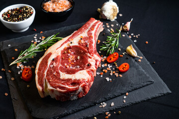 raw meat on a black board with chili, papper, garlic and rosemary